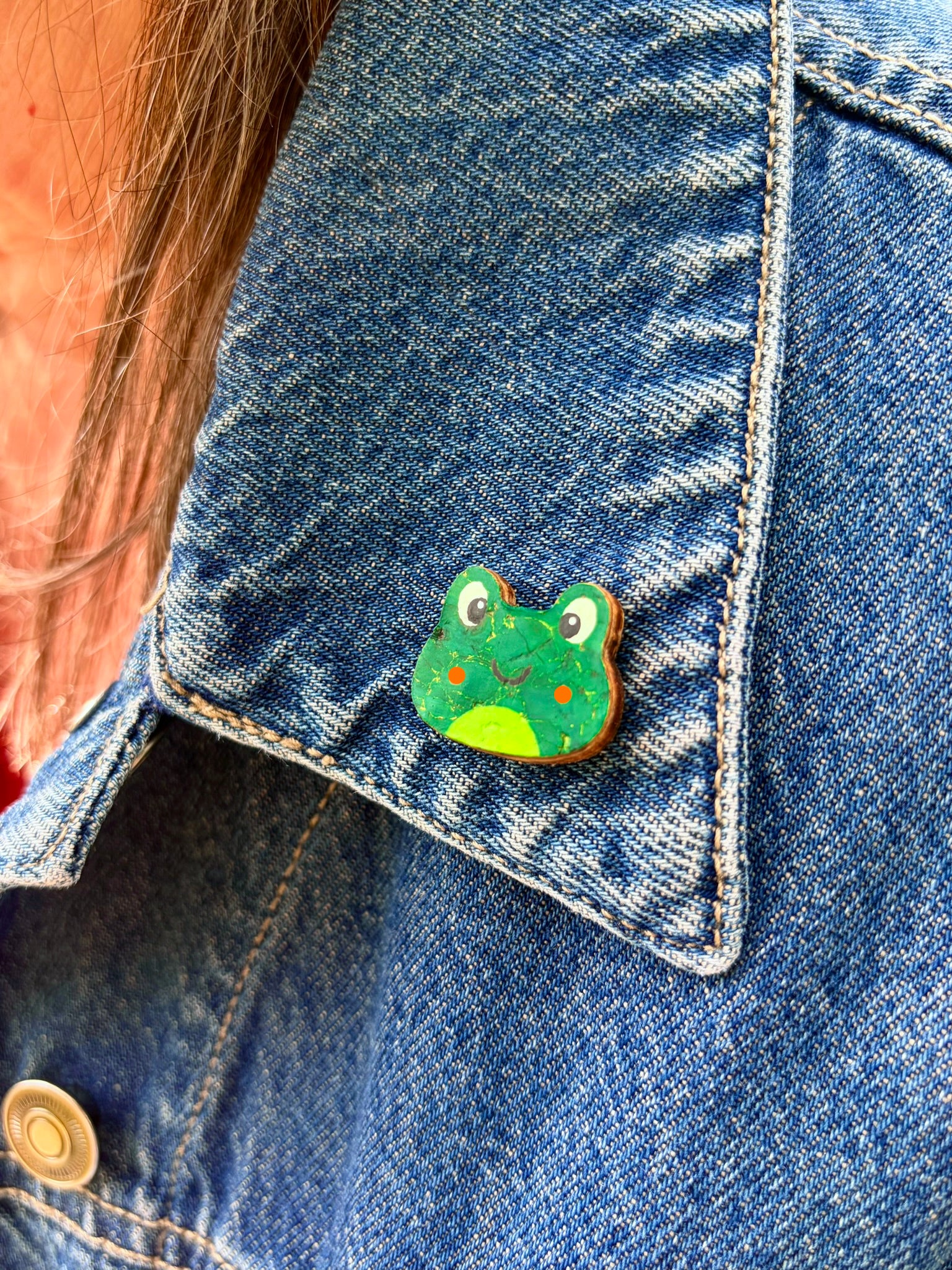 Orange cheeked frog cork pin badge pinned to a denim jacket pocket — handpainted smiley frog, eco-friendly sustainable cork badge handmade in Suffolk UK