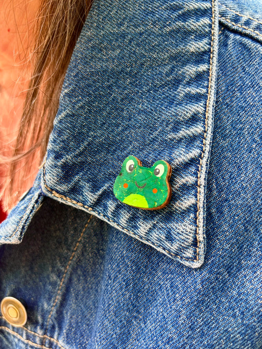 Orange cheeked frog cork pin badge pinned to a denim jacket pocket — handpainted smiley frog, eco-friendly sustainable cork badge handmade in Suffolk UK