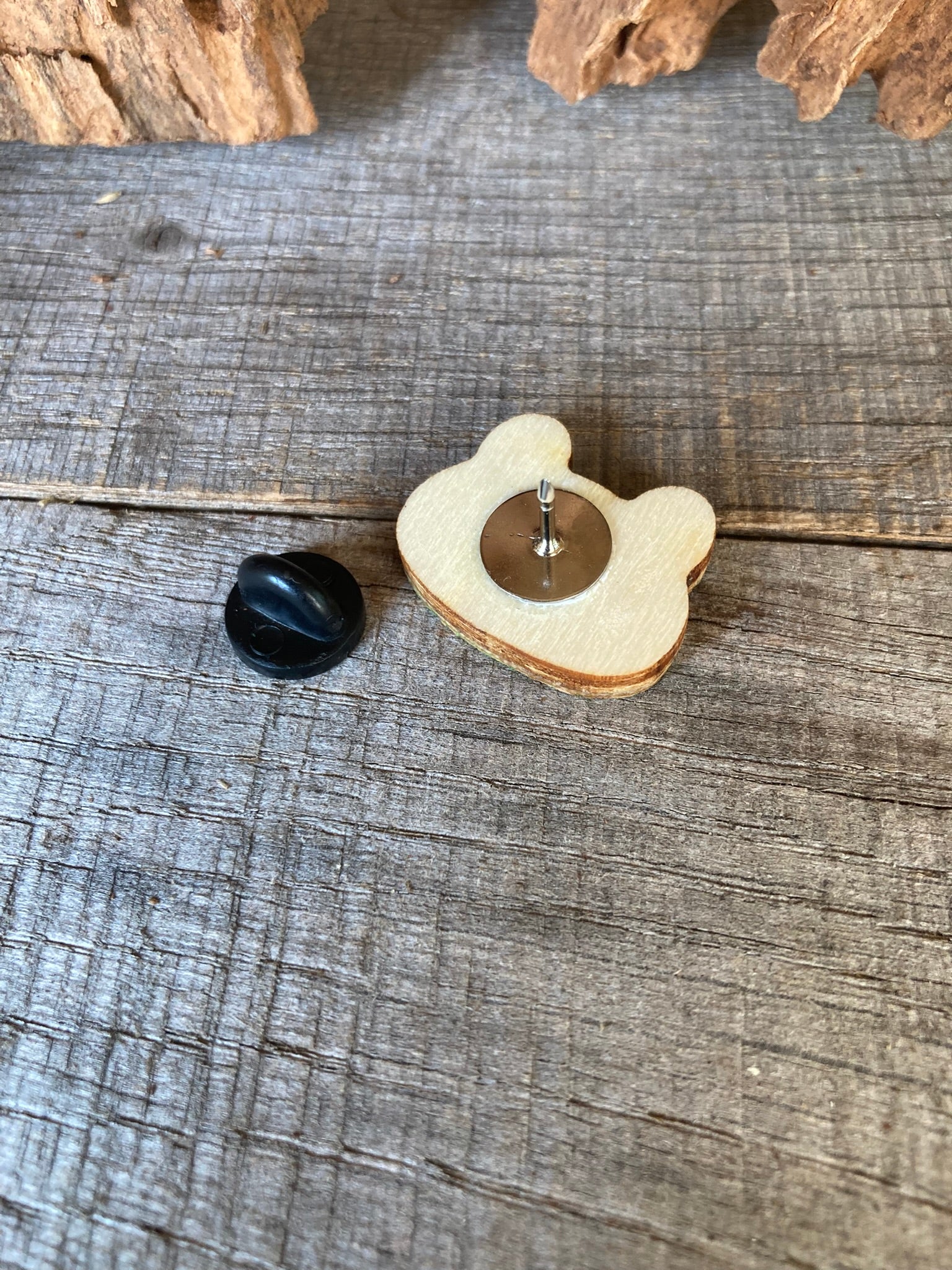 Reverse of the frog cork pin badge on weathered wood showing FSC-certified ply base, metal pin stem and black rubber clasp — secured and finished for everyday wear