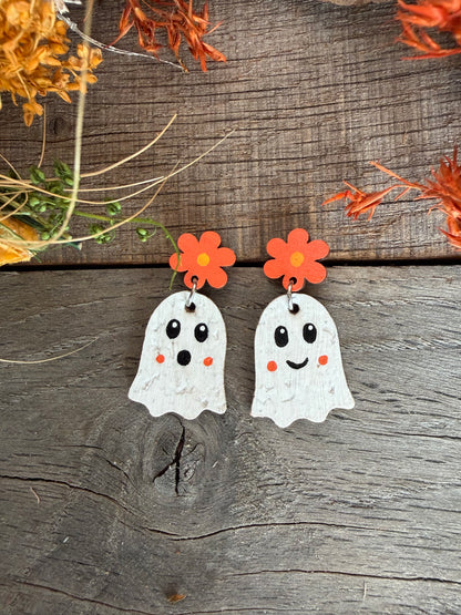 Close-up of orange flower ghost earrings on wood, showing one smiling face and one surprised face.