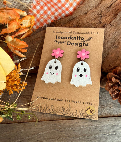White handpainted cork ghosts with pink flower studs and pink cheeks, on a display card beside dried flowers.
