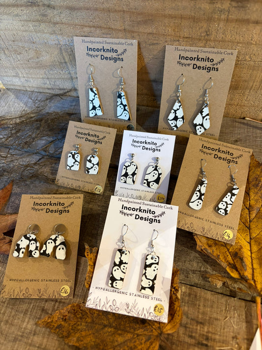 Handpainted ghost-pattern cork earrings in seven designs, displayed on cards with hook and stud-top fastenings among autumn leaves.