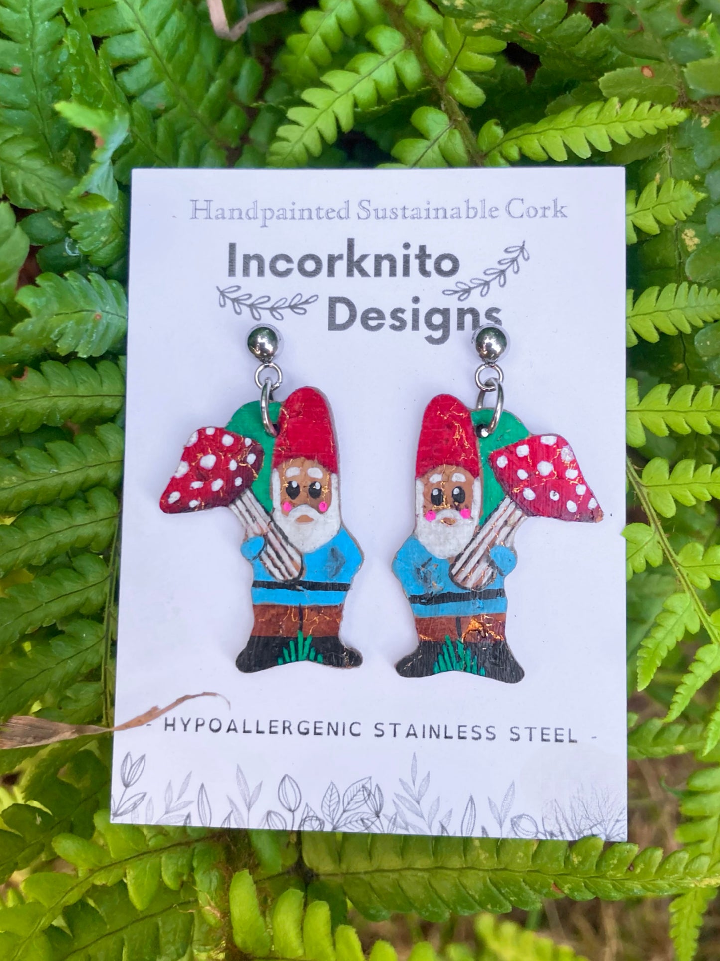 Handpainted gnome and toadstool cork earrings with ball stud fastenings on Incorknito Designs card against green fern background