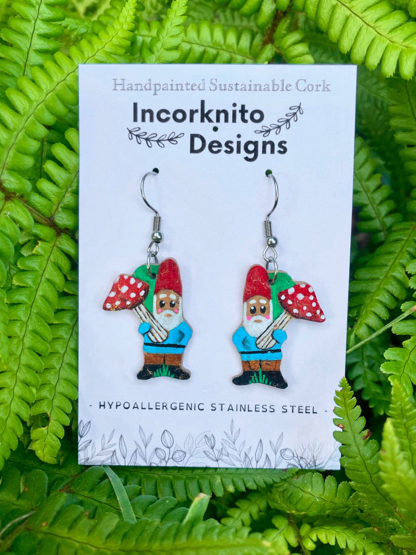 Gnome with toadstool cork earrings on silver hooks on Incorknito Designs branded card against lush green ferns — handpainted sustainable jewellery
