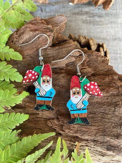 Gnome with toadstool cork earrings on silver hooks resting on weathered wood surrounded by green fern fronds