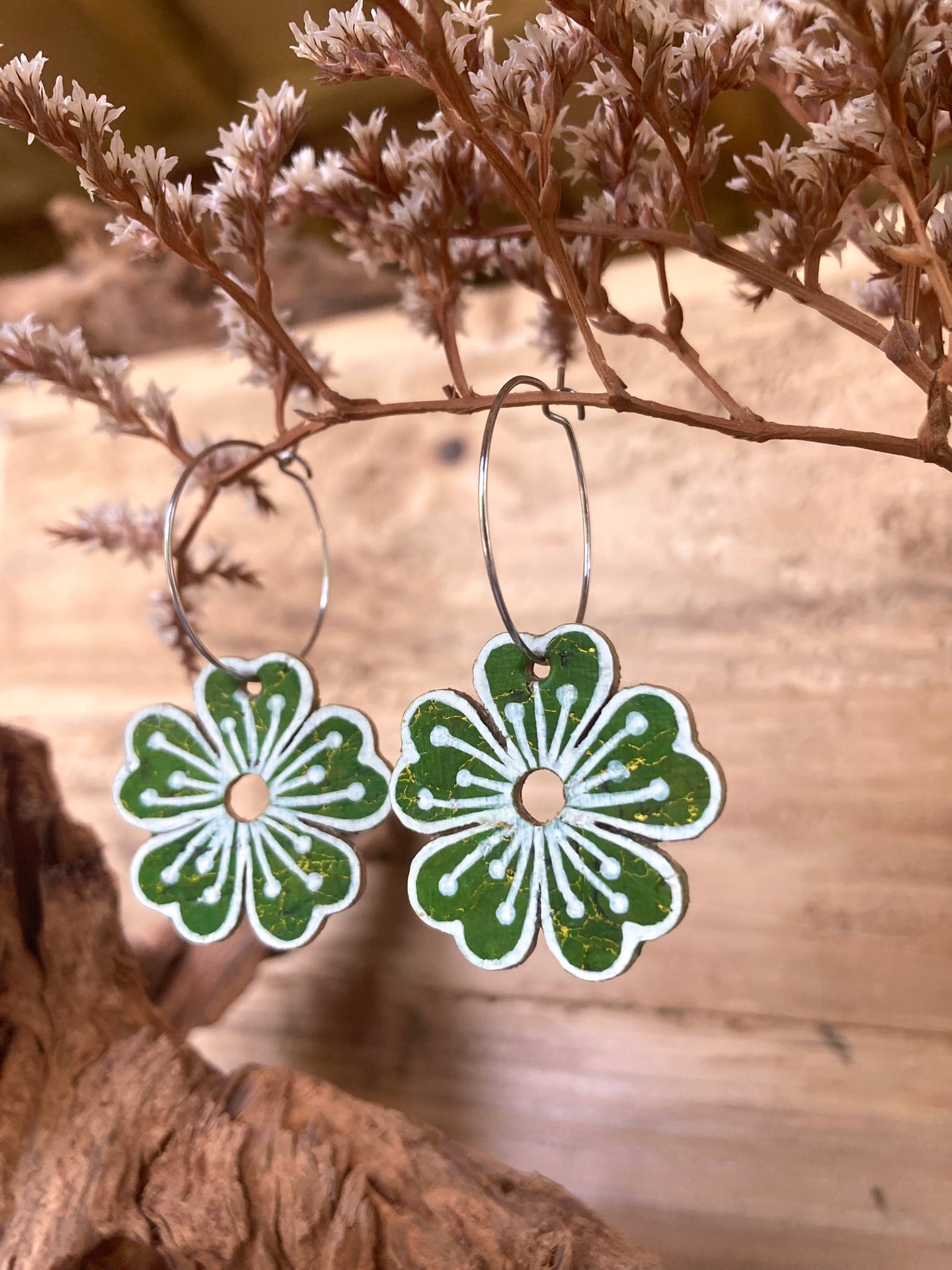 Green large flower cork hoop earrings hanging from a dried botanical branch — silver hoops with handpainted white pollen detail and gold fleck cork
