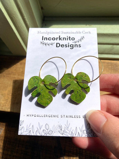 Green monstera cork earrings on gold hoops on Incorknito Designs branded card — handmade sustainable plant jewellery handmade in Suffolk UK