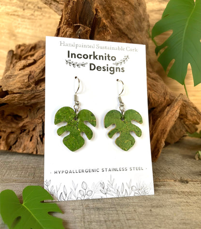 Green monstera cork earrings on silver hooks on Incorknito Designs branded card propped against driftwood with monstera leaves — hypoallergenic sustainable jewellery