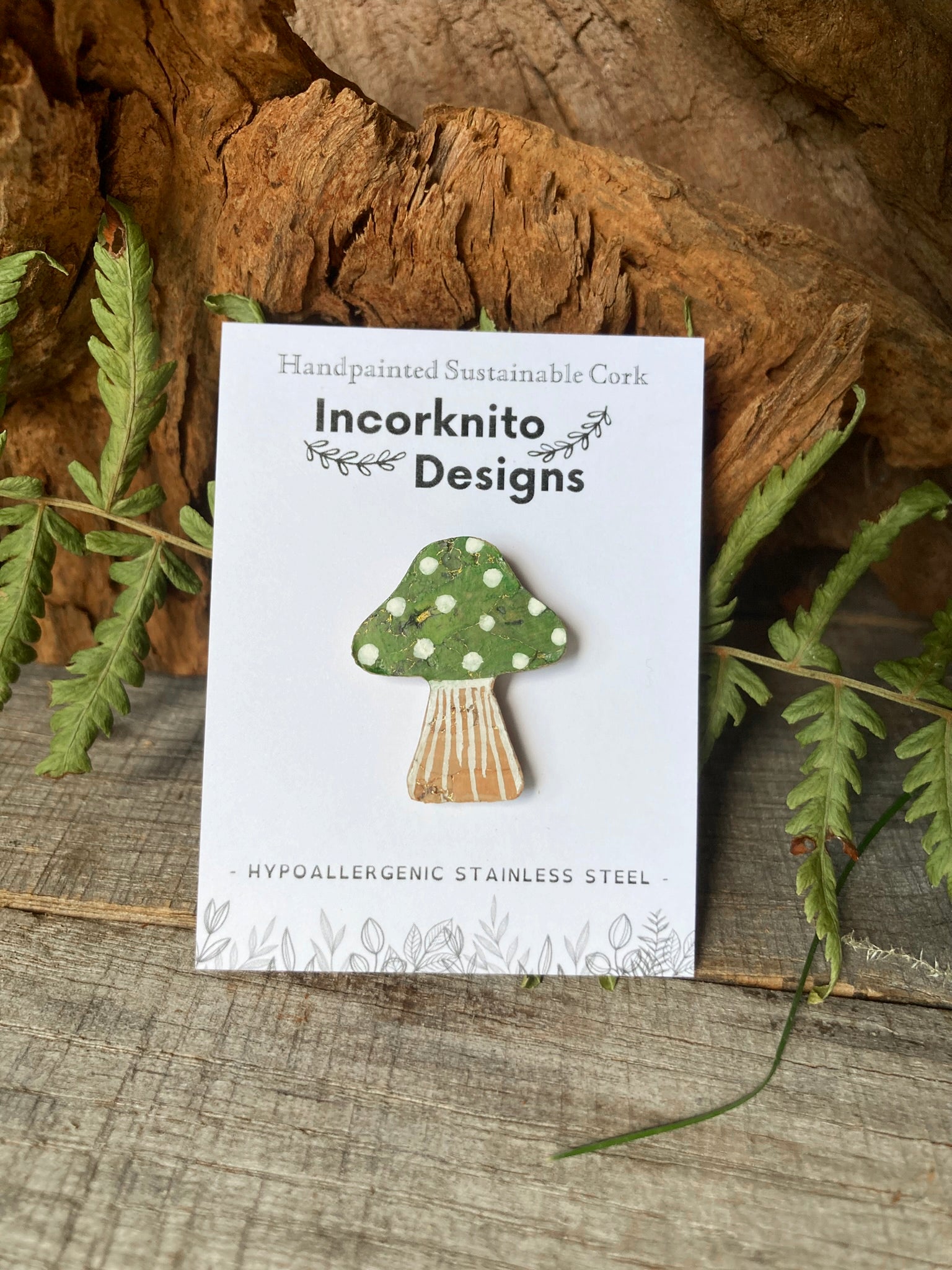 Green toadstool cork pin badge on Incorknito Designs branded card with green fern fronds and driftwood — handpainted sustainable woodland badge