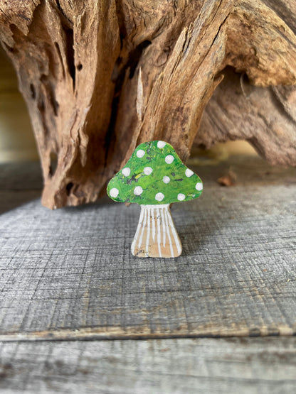Close-up of handpainted green toadstool cork pin badge on weathered wood — white spot detailing and gold fleck shimmer on rich woodland green cap