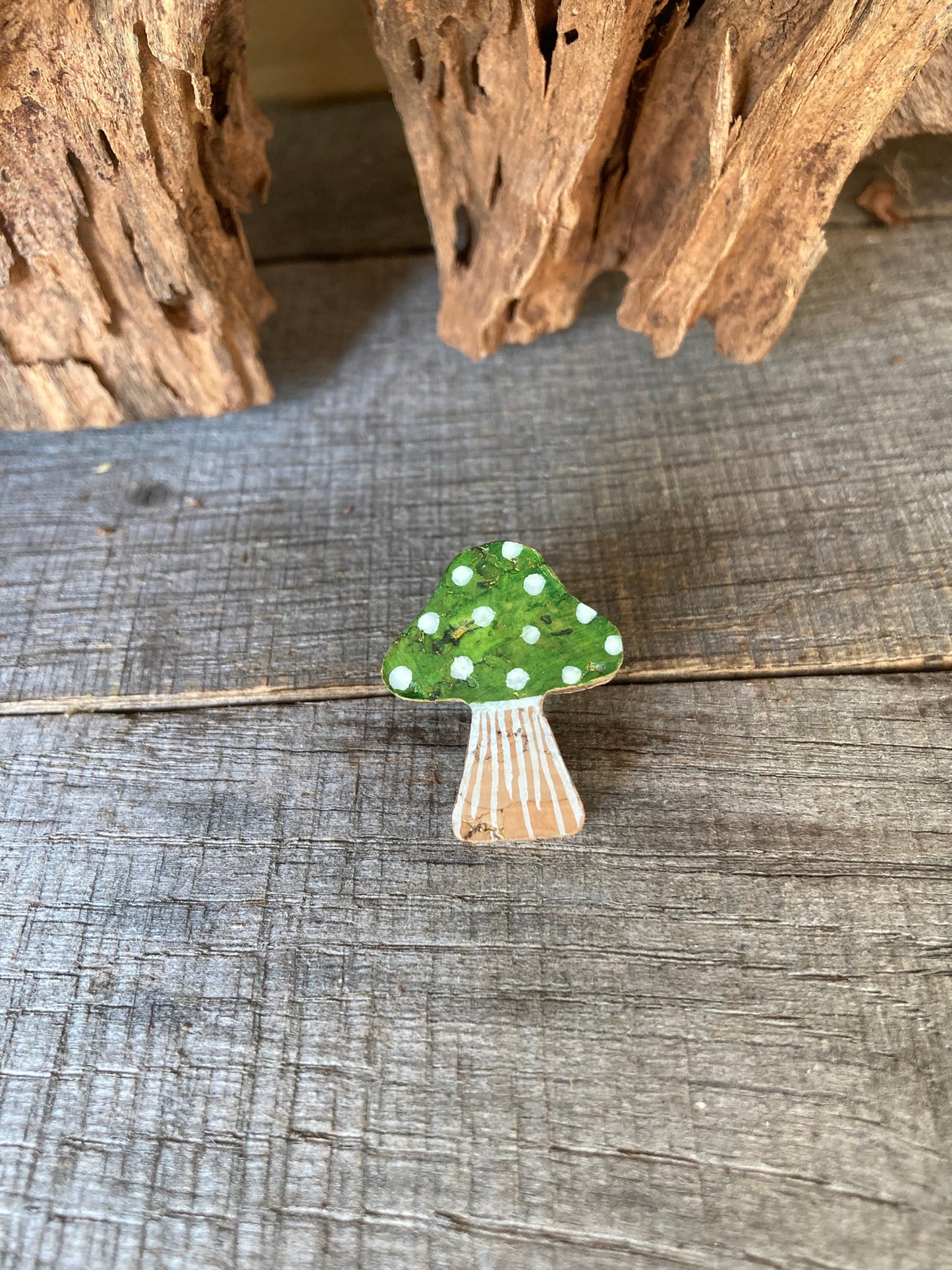 Green toadstool cork pin badge flat lay on weathered grey wood — natural cork stem with fine line detail and rich woodland green spotted cap