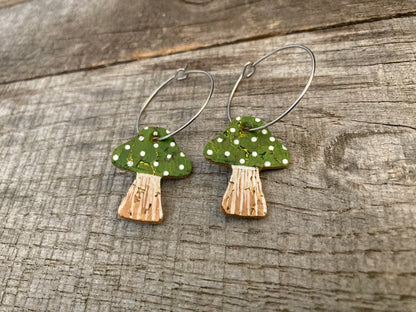 Green toadstool cork large hoop earrings flat lay on plain weathered wood — close-up showing the gold fleck cork and handpainted green cap on silver hoops