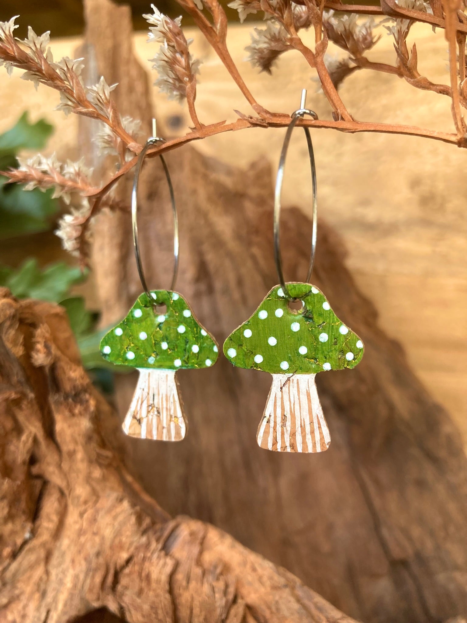 Green toadstool cork large hoop earrings hanging from a dried branch — silver hoops with handpainted green cap and white polka dots