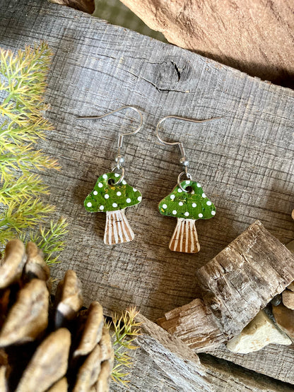 Green toadstool cork medium earrings flat lay on weathered wood with moss and pine cone — handpainted green cap with white polka dots, handmade in Suffolk UK