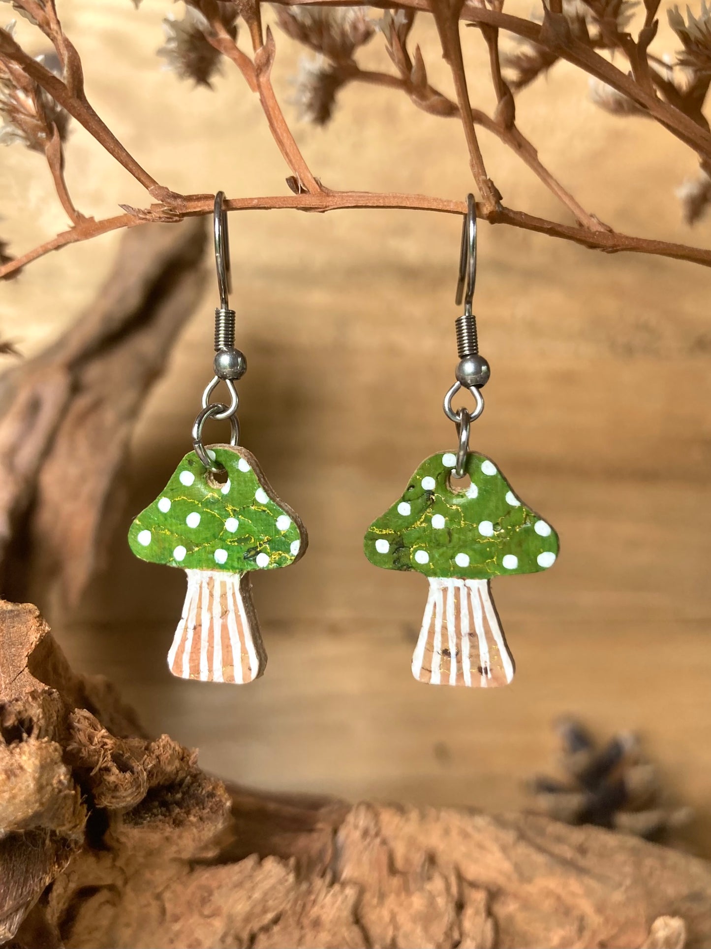 Green toadstool cork medium earrings hanging from a dried branch — silver hooks with handpainted green cap and white spot detail