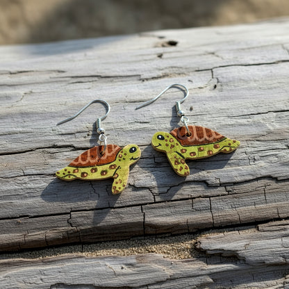 Green sea turtle earrings on silver hooks resting on weathered driftwood — handpainted sustainable cork by Incorknito Designs