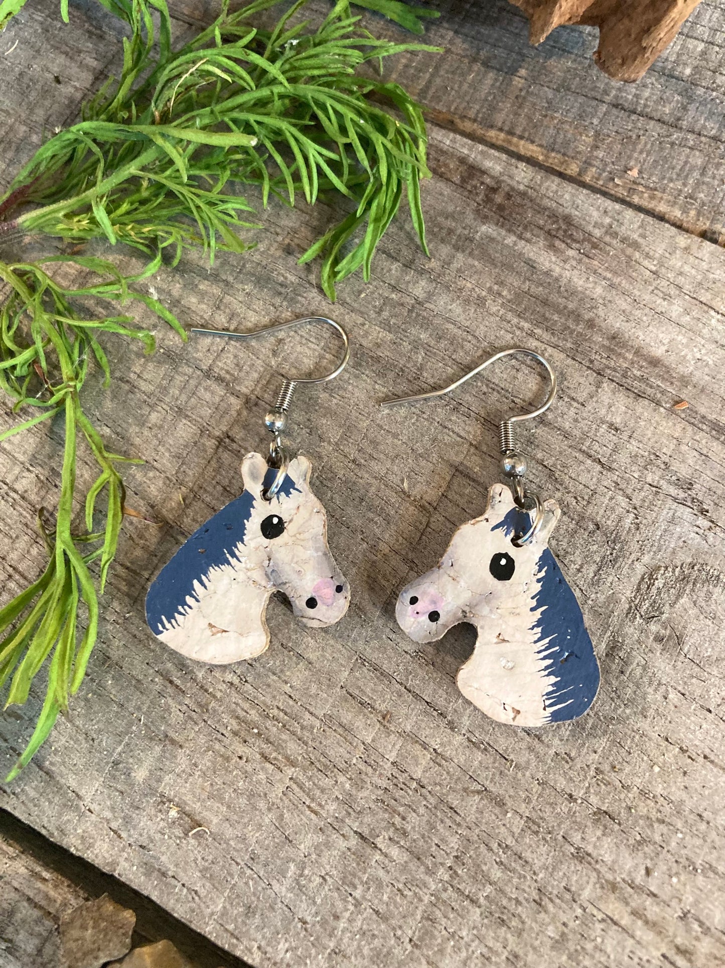 Grey and white horse cork earrings on silver hooks flat lay on wooden surface with greenery — handpainted sustainable cork jewellery Suffolk UK
