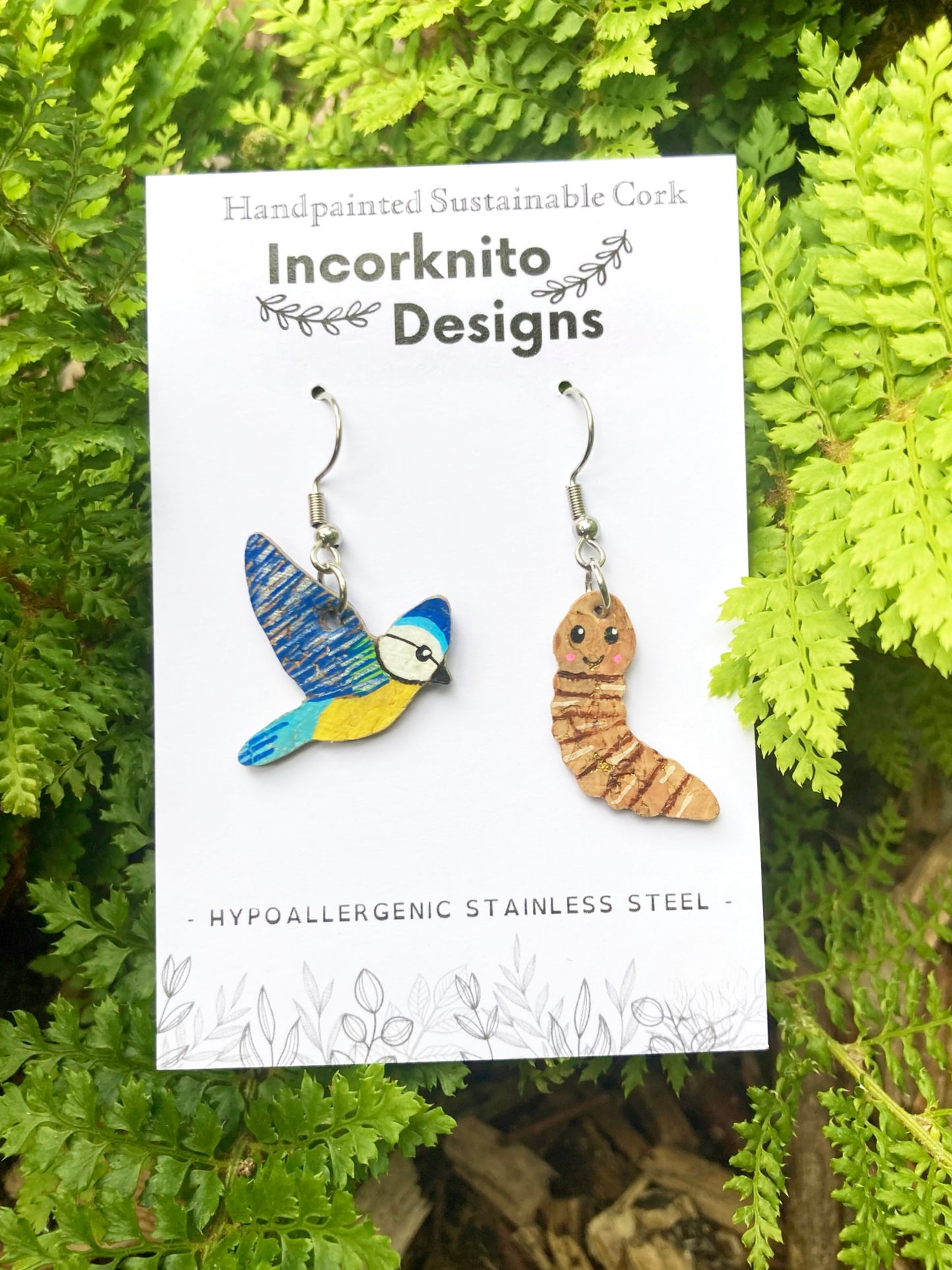 Blue tit and worm cork earrings on branded card with green fern background