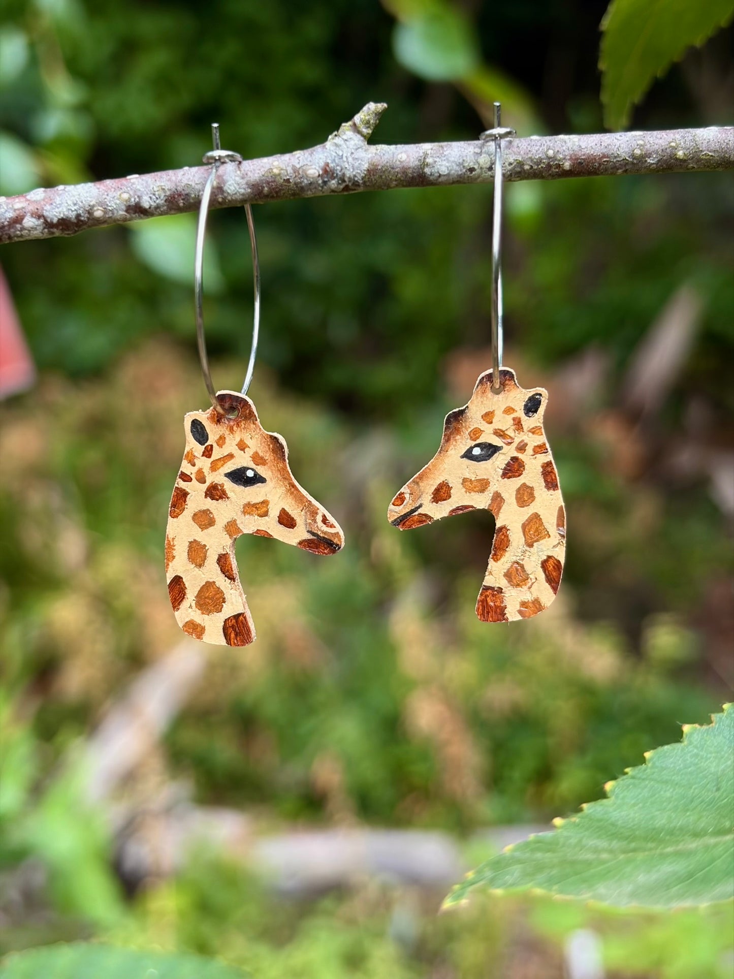 Handpainted giraffe cork earrings made from sustainable cork leather hanging from branch 
