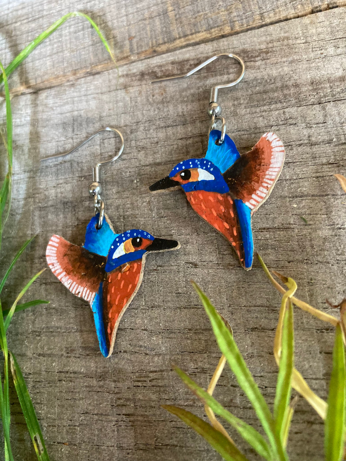 Handpainted kingfisher cork earrings on silver hooks on weathered wood with russet and green grass — British wildlife cork jewellery