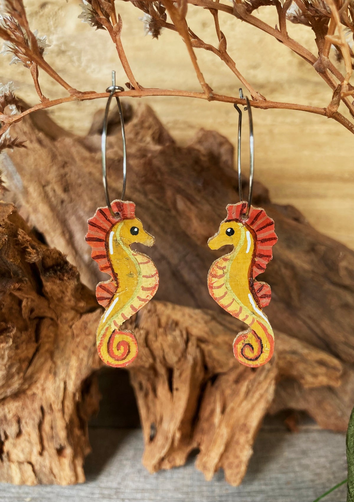 Handpainted seahorse cork earrings on silver hoops hanging from driftwood — eco-friendly ocean jewellery handmade in Suffolk UK