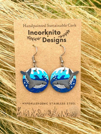 Handpainted humpback whale cork earrings on silver hooks on Incorknito Designs branded card against golden dried grass — eco-friendly ocean jewellery