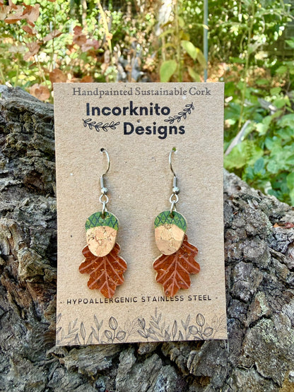 Acorn and oak leaf cork earrings in green colourway on Incorknito Designs card, propped against textured cork bark with autumn foliage
