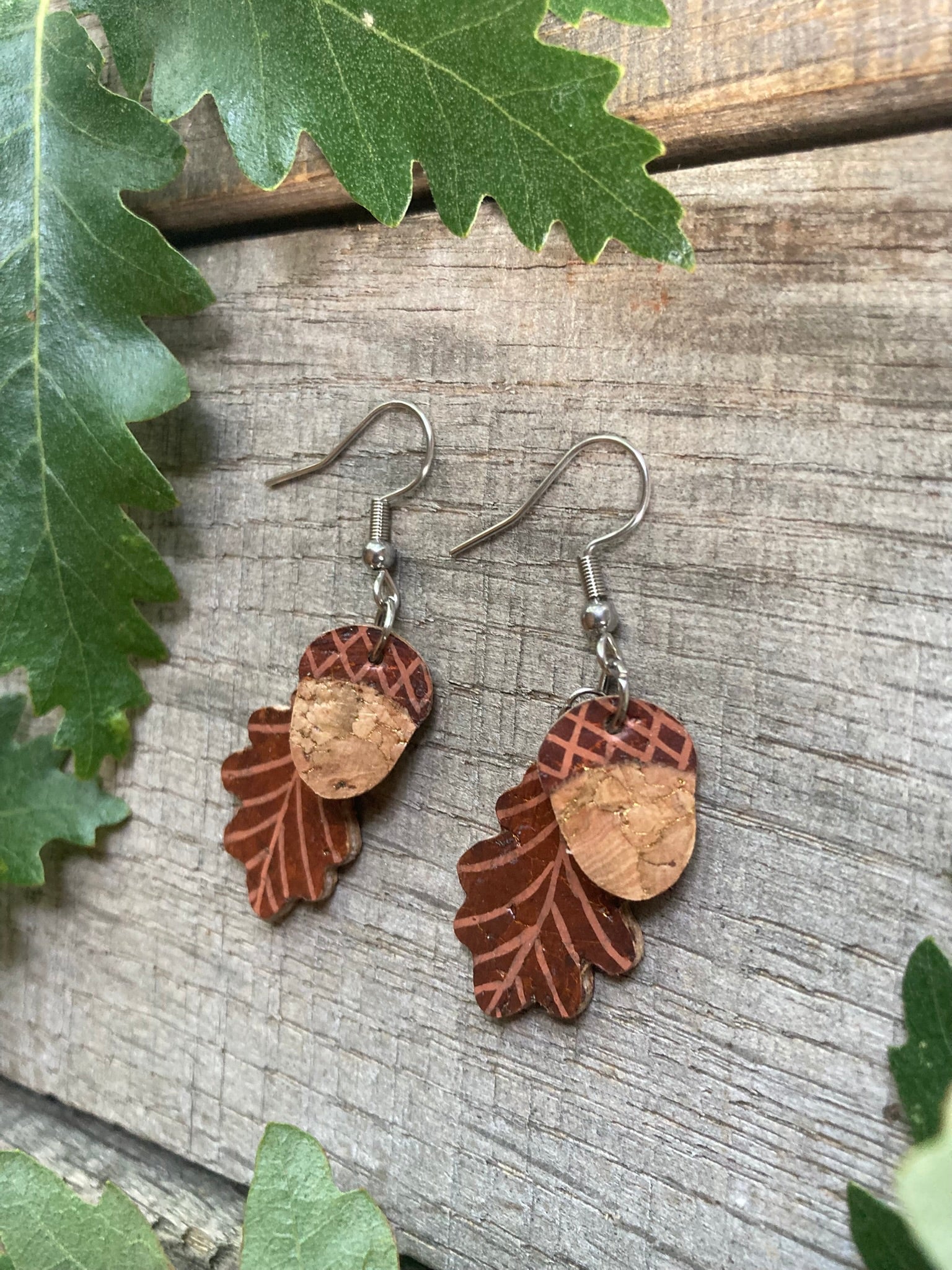 Cork acorn and oak leaf earrings in green colourway flat lay on weathered wood surrounded by real oak leaves