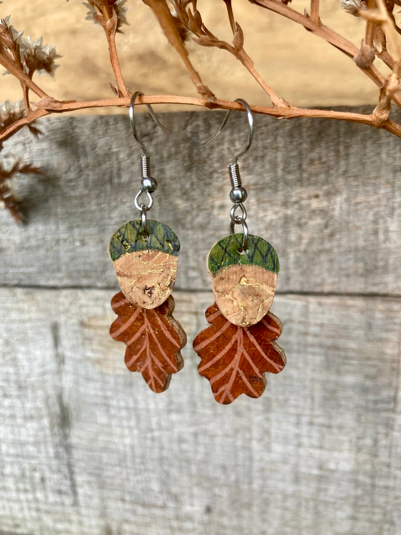 Acorn and oak leaf cork dangle earrings in green colourway hanging against a rustic weathered wood background