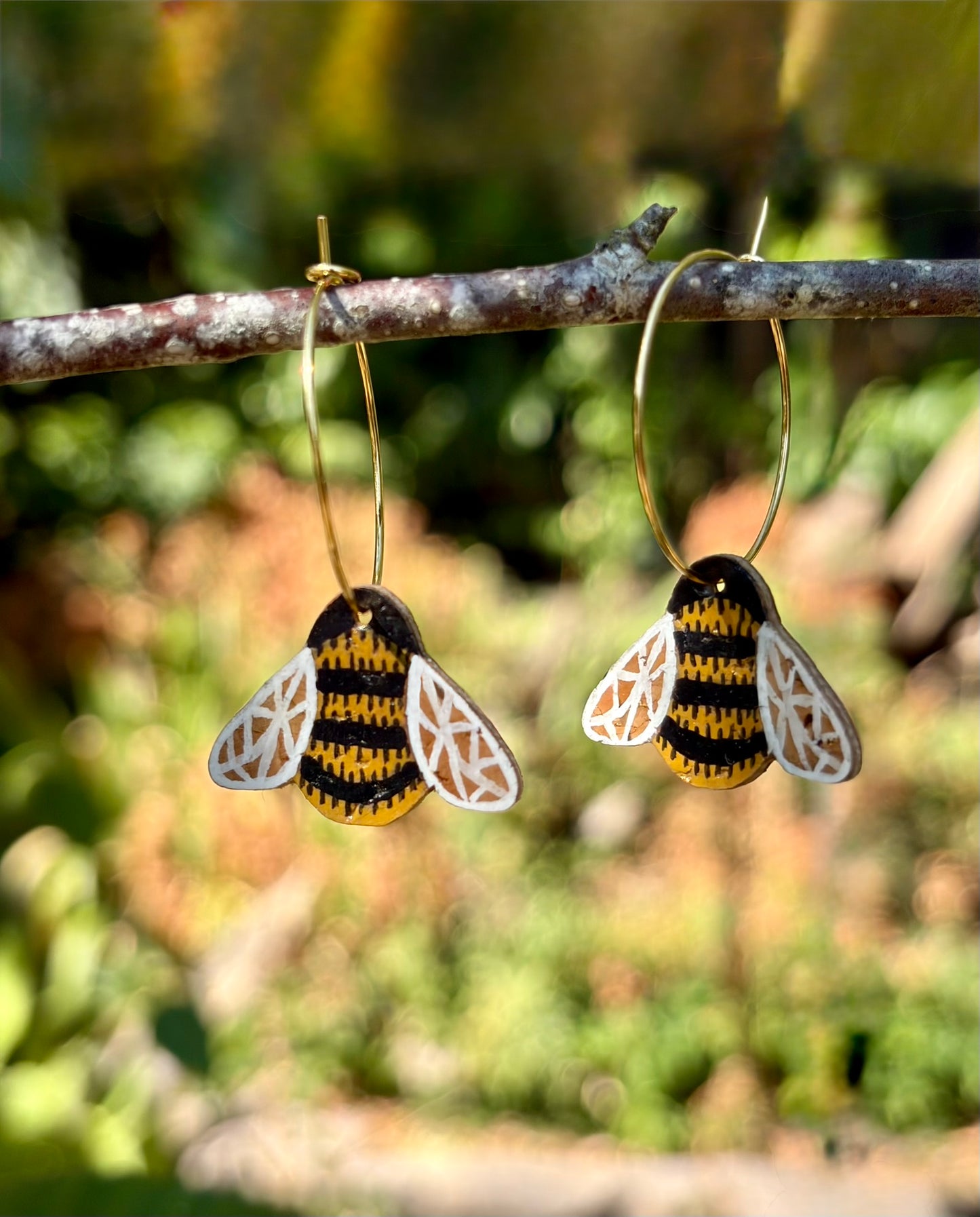 Cork bumblebee earrings with silver hook fastening on Incorknito Designs card, held against a green hedge