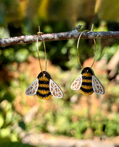 Cork bumblebee earrings with silver hook fastening on Incorknito Designs card, held against a green hedge
