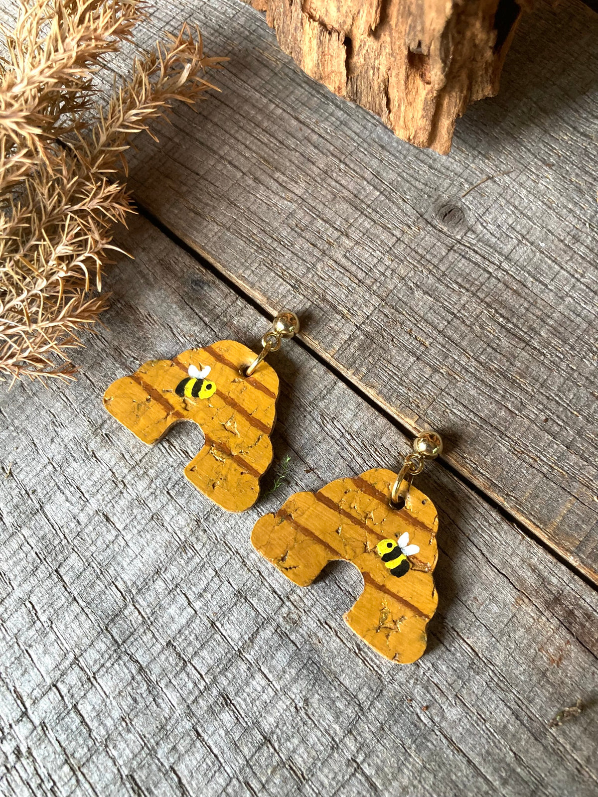 Cork beehive earrings with gold ball stud fastening, flat lay on weathered wood with dried golden pampas grass