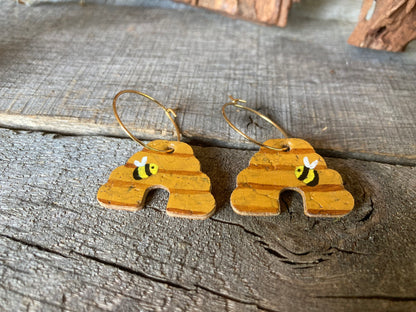 Handpainted cork beehive earrings on gold hoops, close up flat lay on weathered wood showing bumblebee and horizontal band detail