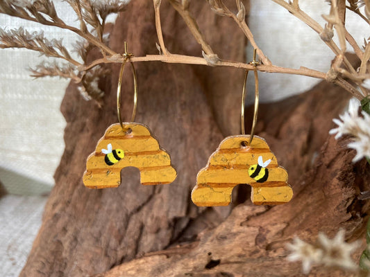 Handpainted cork beehive earrings on gold hoops, hanging from a dried branch with cork bark and dried white flowers