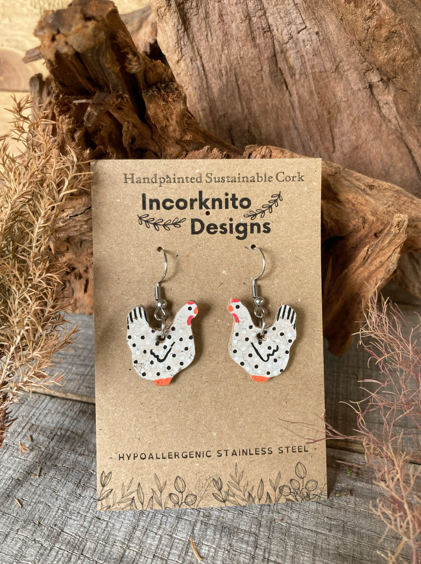 Handpainted black and white cork chicken earrings on silver hooks, displayed on Incorknito Designs branded card with cork bark and dried botanicals background