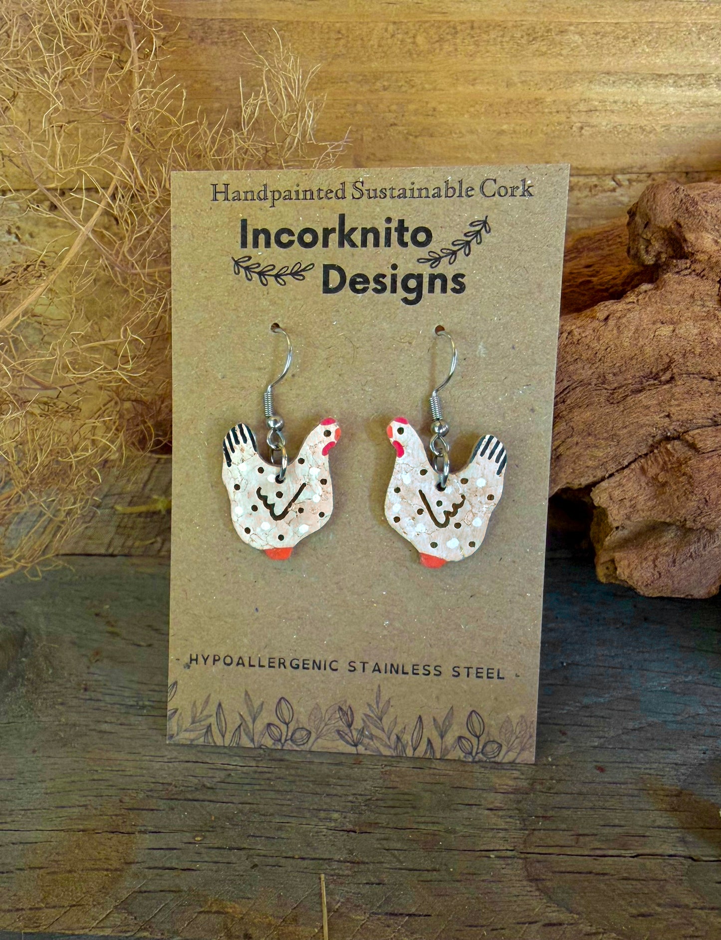 Handpainted black and white cork chicken earrings on silver hooks, displayed on Incorknito Designs branded card with dried grass and cork bark background