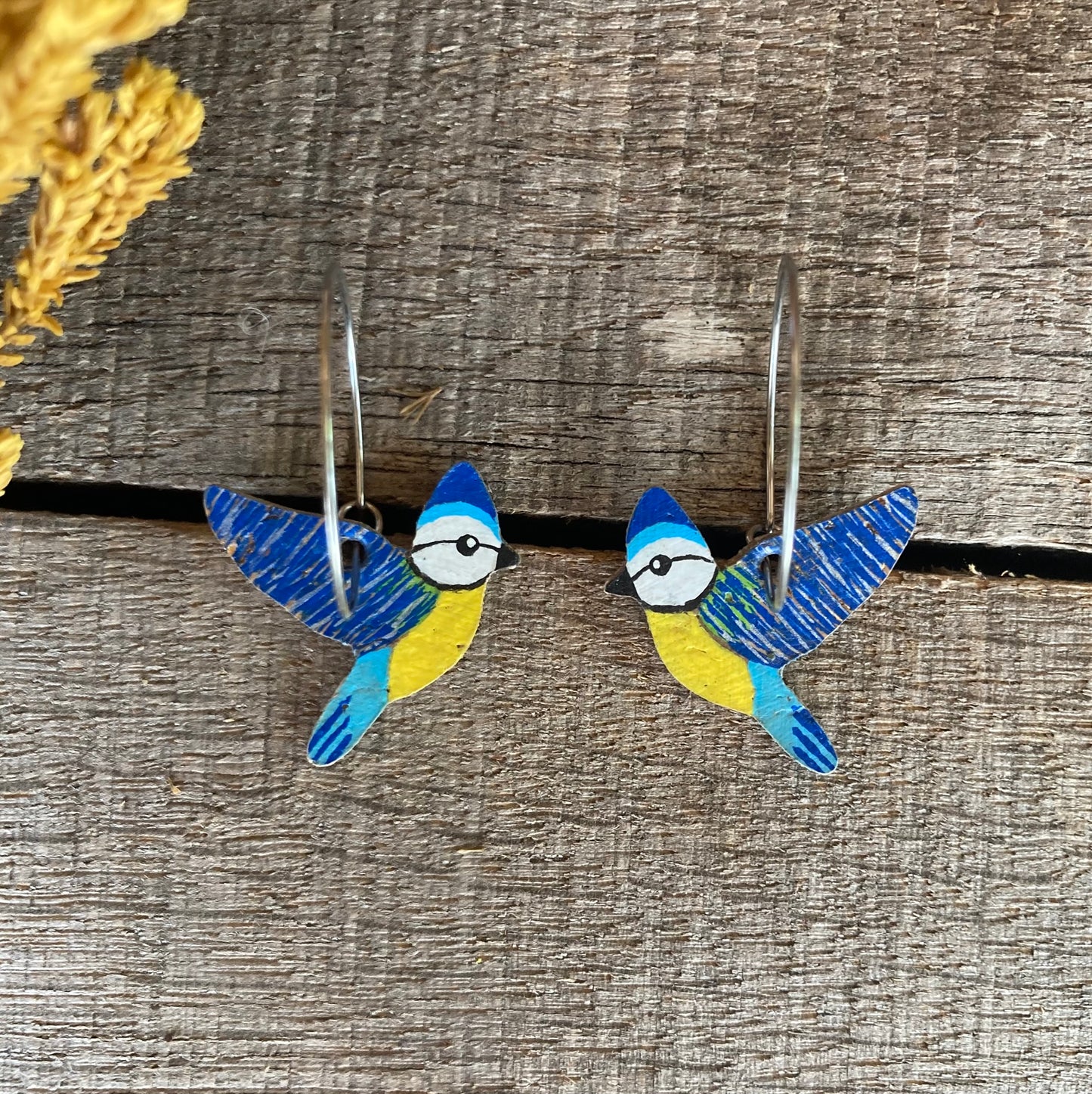 Blue tit cork hoop earrings, handpainted, flat lay on weathered wood