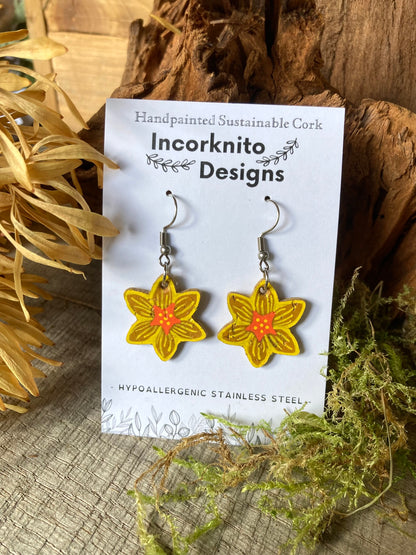 Cork daffodil hook earrings on an Incorknito Designs card, styled with driftwood and dried moss.