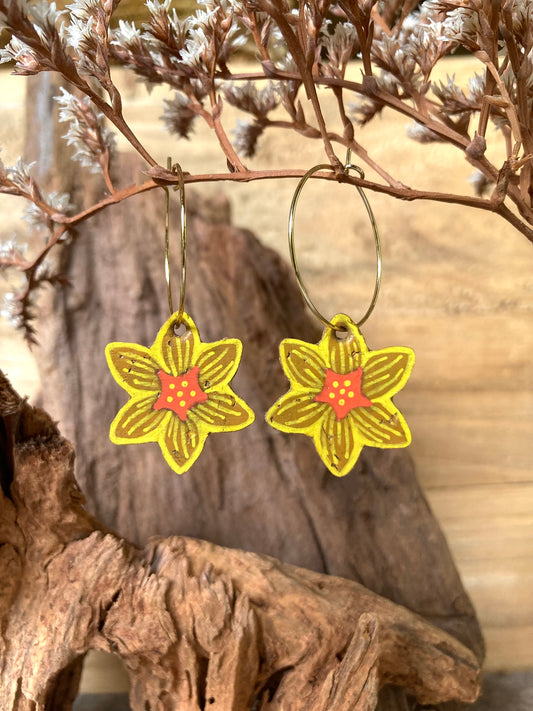 Handpainted cork daffodil hoop earrings hanging from a driftwood branch against a warm natural background.