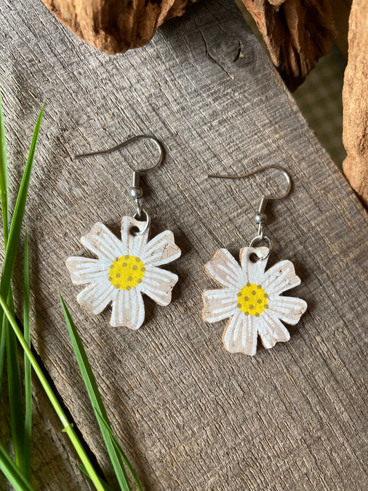 Handpainted cork daisy earrings on silver hooks, flat lay on weathered wood with green grass and driftwood