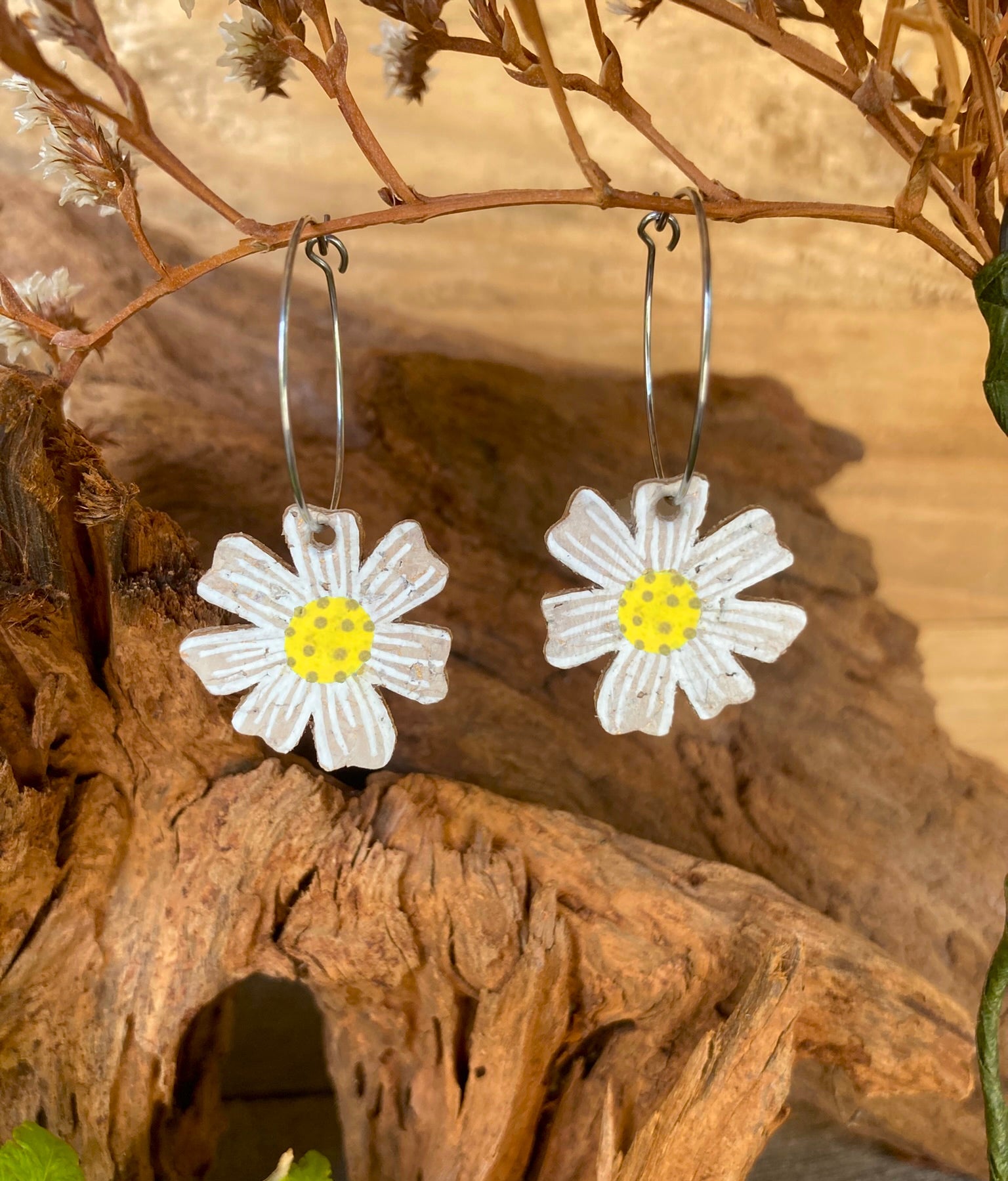 Cork daisy earrings on silver hoops, hanging from a dried branch with warm driftwood background