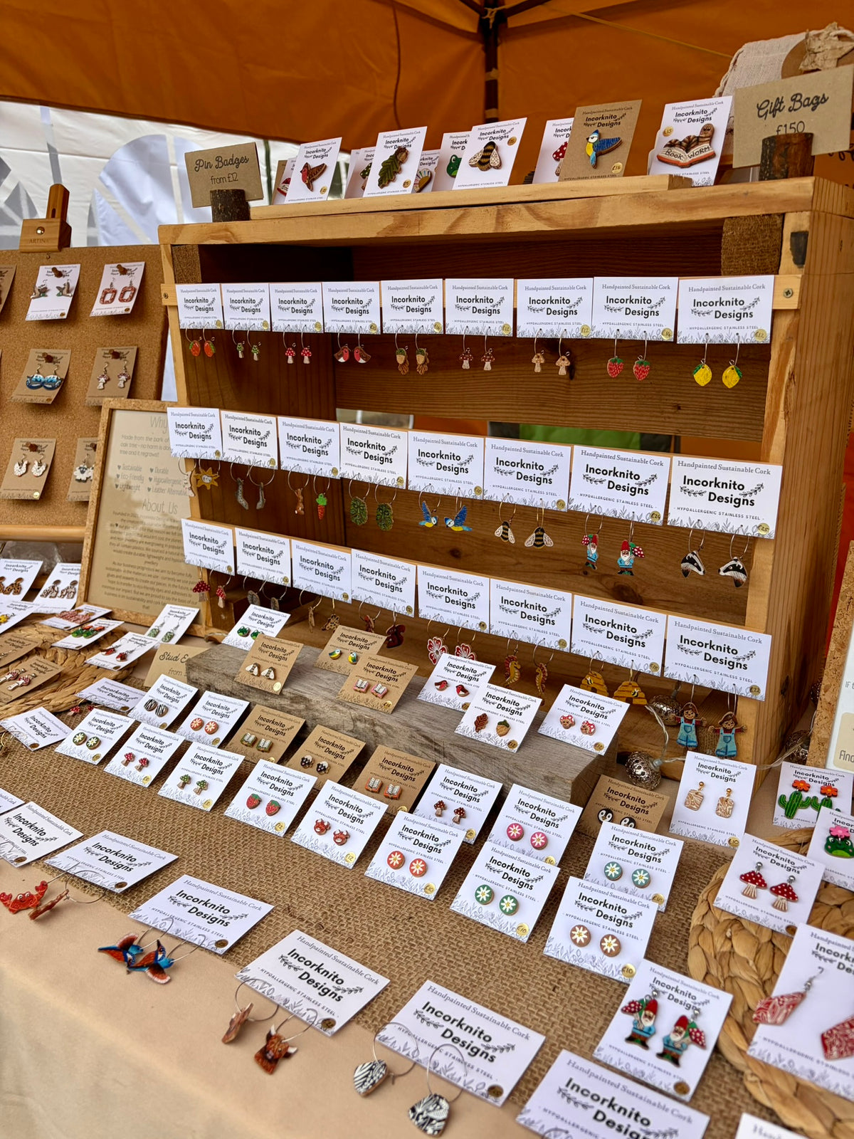 Market stall of Incorknito Designs earrings displayed on a range of wooden backgrounds at a craft market
