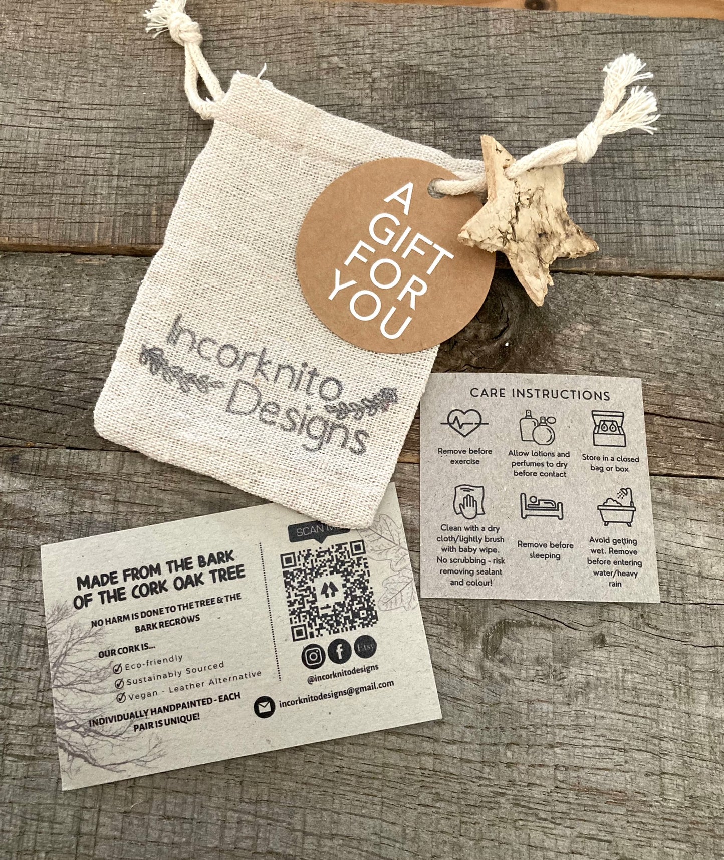 Incorknito Designs branded hessian gift bag with kraft "A Gift For You" tag, bark star charm, care card and cork about card laid out on weathered wood