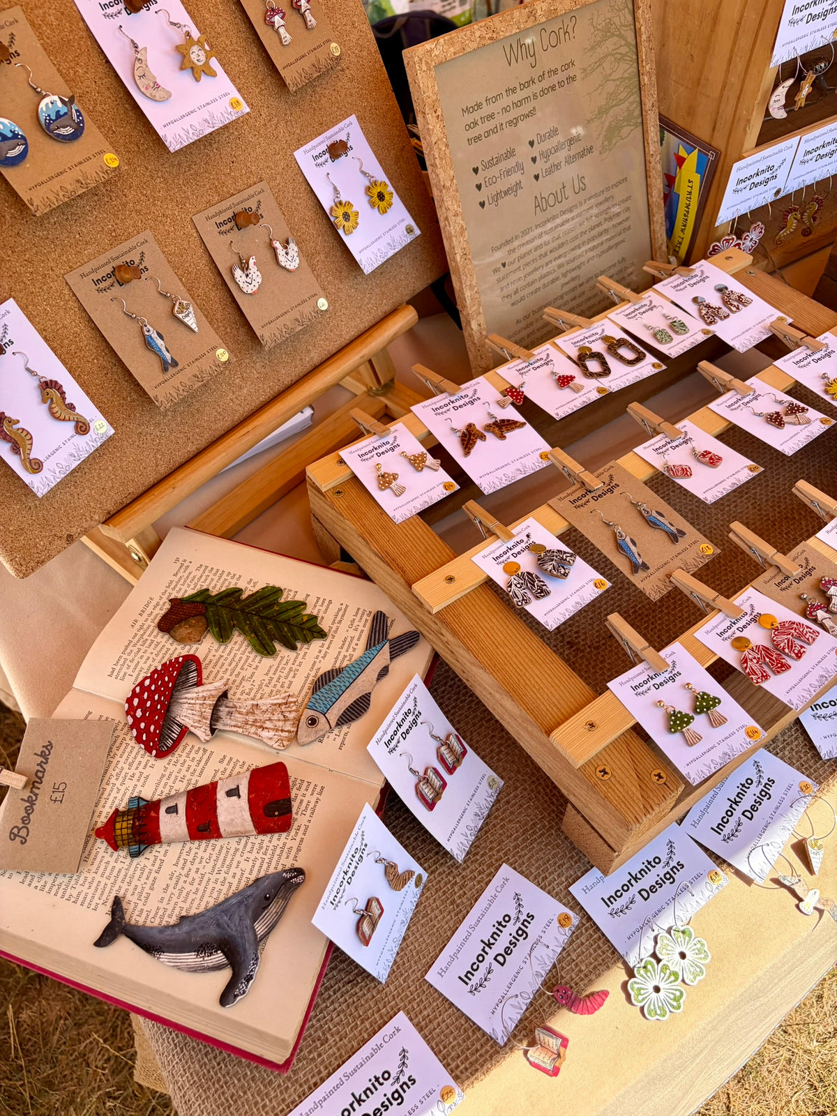 Close up shots of handpainted cork earrings and bookmarks laid out on a table on a book and hessian fabric