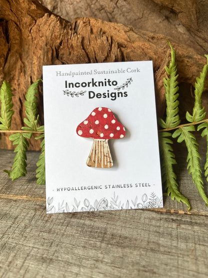 Red fly agaric toadstool cork pin badge on Incorknito Designs branded backing card, surrounded by fern leaves and cork bark — handpainted sustainable cork, hypoallergenic stainless steel