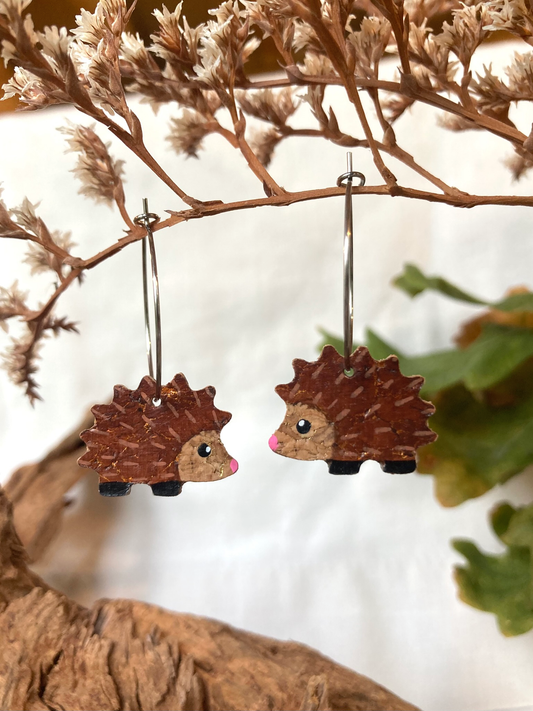 Handpainted cork hedgehog earrings hanging from a dried branch — rich brown with gold fleck spines and pink nose