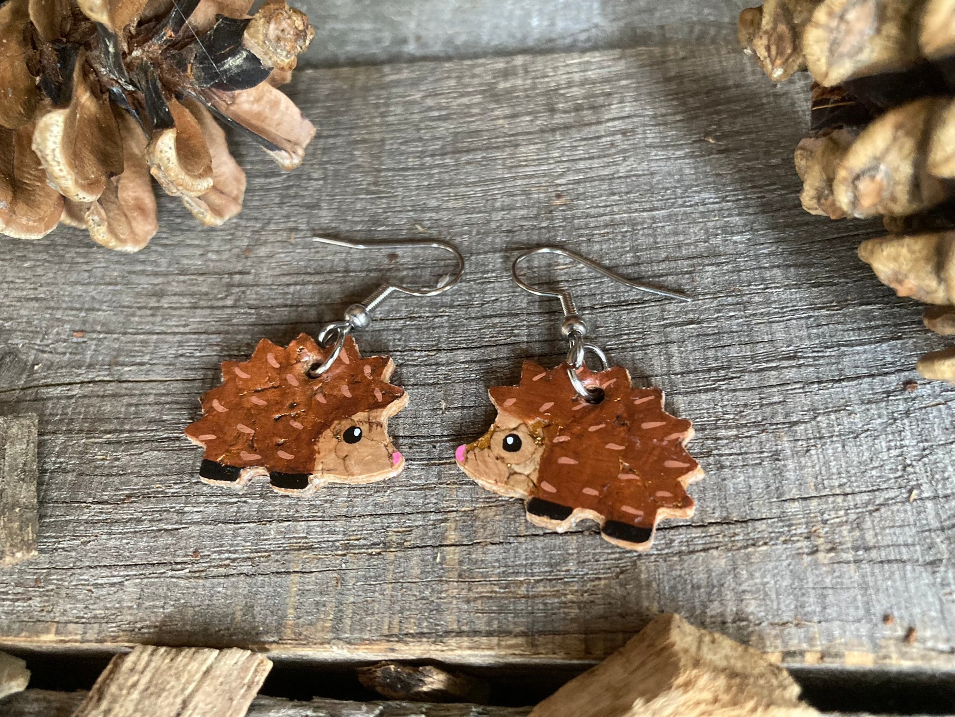 Sustainable cork earrings in the shape of hedgehogs with bright eyes and pink nose with little black feet and brown prickles