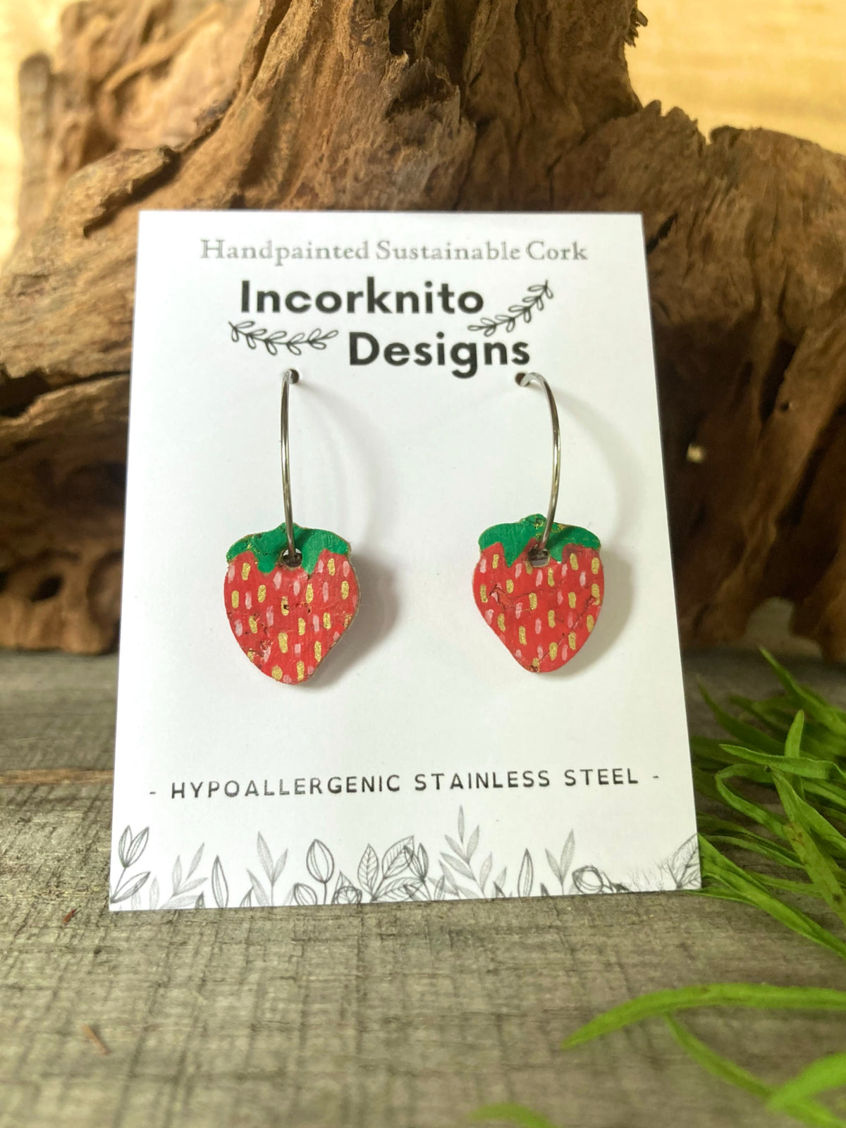 Handpainted mini strawberry cork earrings on silver open-back hoops, displayed on Incorknito Designs branded card with cork bark background