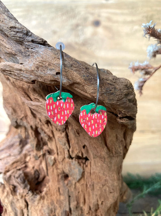 Cork mini strawberry earrings on silver open-back hoops, hanging from cork bark with dried botanicals background