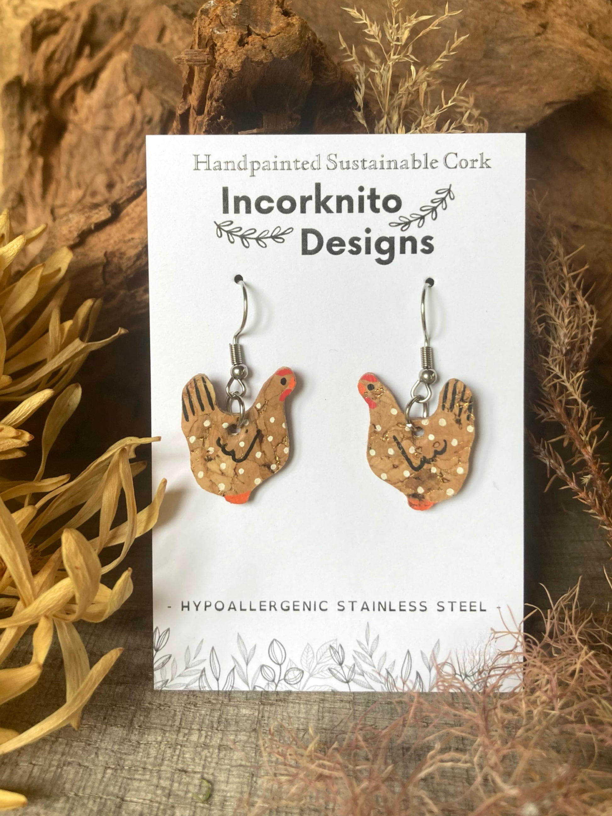 Handpainted natural cork chicken earrings on silver hooks, displayed on Incorknito Designs branded card with cork bark and dried botanicals background